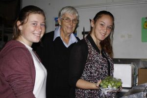 Tin Can Bay IGA's Ruth Steinsch trains Ally Duckworth and Paige Edmonds in the wrapping machine to keep produce well-presented and fresh - the girls also learnt to use the cash register, packing shelves and what goes on behind the scenes