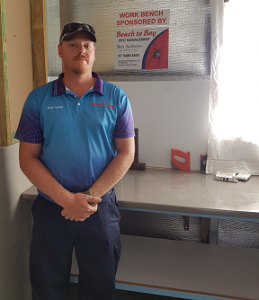 Ben Andrews of Beach to Bay Pest Management proudly standing in front of the workbench his company sponsored 